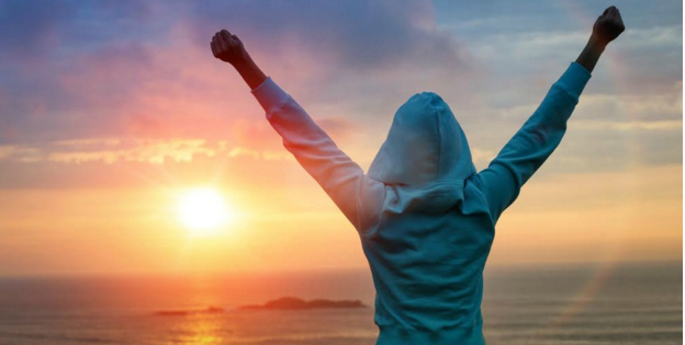 person with hood up raising arms