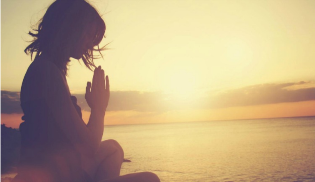 person meditating near the ocean during sunset