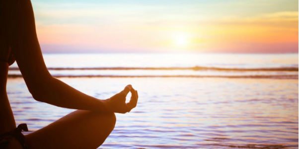 Person meditating near water during sunset